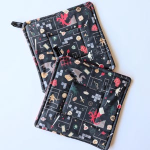 May include: Two black and red quilted pot holders with a Dungeons and Dragons theme. The pot holders feature a repeating pattern of dice, swords, dragons, and other fantasy elements.