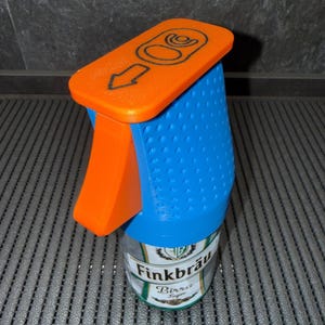 May include: An orange and blue can-shaped spray bottle. The top is orange with a black arrow and graphic. The blue body has a textured surface. The can reads "Finkbräu Birra".