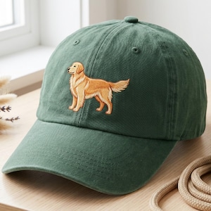 May include: A dark green baseball cap with an embroidered golden retriever dog. The cap has a curved peak and a fabric strap. The dog is in shades of tan and brown.