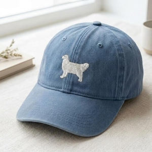 Peut inclure: Une casquette de baseball bleue avec une broderie blanche représentant un chien debout de profil sur le panneau avant. La casquette présente une visière incurvée, un bouton sur le dessus et des œillets cousus pour la ventilation.