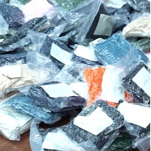 May include: A large collection of assorted apparel items individually packaged in clear plastic bags. Each bag features a white rectangular label on the front. The items vary in color, including black, white, orange, green, and beige fabric.