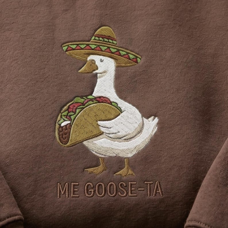 May include: Brown sweatshirt with an embroidered design of a white goose wearing a sombrero and holding a taco. The text "ME GOOSE-TA" is embroidered below the goose.