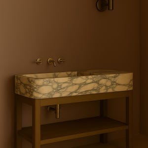 May include: A rectangular marble sink with a veined pattern, set on a bronze-colored metal frame with a lower shelf. The sink has bronze fixtures and is mounted against a brown wall. A matching sconce is mounted on the wall.