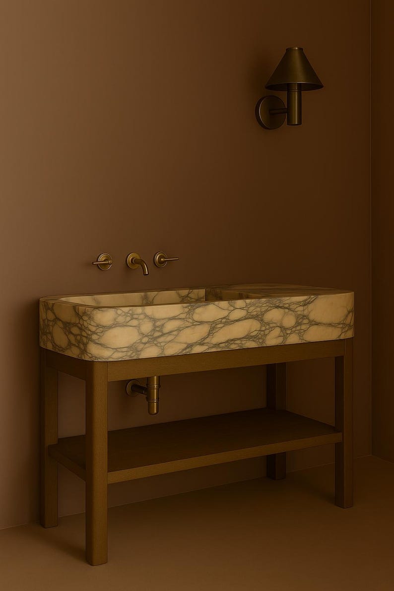 May include: A rectangular marble sink with a veined pattern, set on a bronze-colored metal frame with a lower shelf. The sink has bronze fixtures and is mounted against a brown wall. A matching sconce is mounted on the wall.