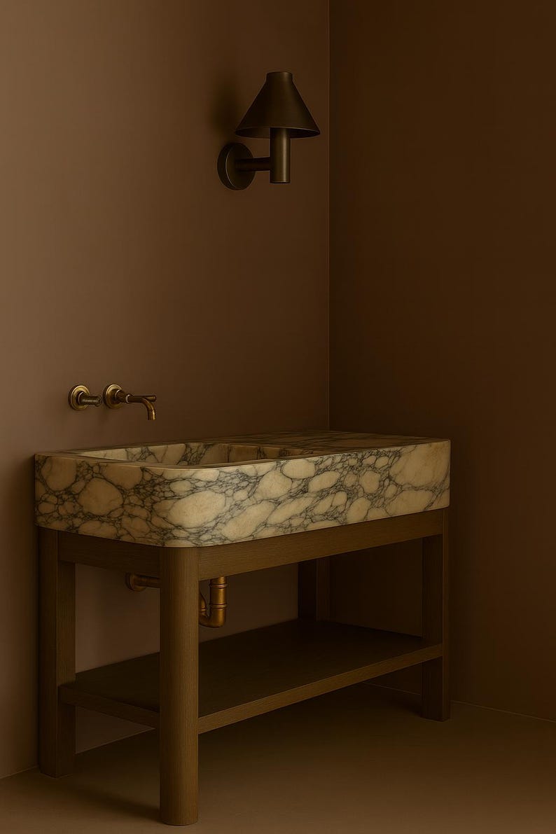 May include: A marble sink with a light brown and gray pattern sits on a wooden stand with a lower shelf. The sink has a brass faucet and is mounted against a brown wall. A matching wall sconce is above the sink.