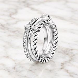 May include: A silver-toned multi-band ring featuring three distinct layers: one band with a twisted rope texture, one smooth polished band, and one band encrusted with small clear stones, all connected by a small silver-toned metal loop.