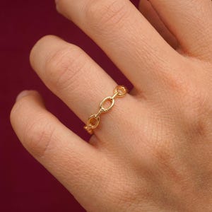 Peut inclure: Une bague dorée composée d'une série de maillons ovales interconnectés avec une texture de corde torsadée. L'anneau est formé de formes circulaires et ovales répétitives, créant un design en chaîne continu qui entoure le doigt avec une finition polie.