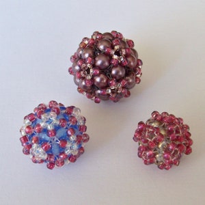 May include: Three beaded spheres in different sizes. The largest sphere is a deep purple colour, the medium sphere is blue and white, and the smallest sphere is a deep red colour.