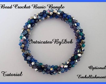 May include: A blue and silver beaded crochet bangle bracelet. The bracelet is made with small, faceted beads in shades of blue, teal, and silver. The bracelet is twisted and has a simple, elegant design. The text "Intricates By Deb" is visible in the center of the bracelet.
