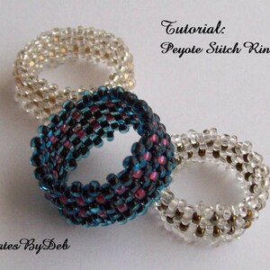 May include: Three beaded rings in different colors. The rings are made with a peyote stitch technique. The rings are white, clear, and blue with pink accents. The text "Tutorial: Peyote Stitch Ring" is visible in the image.