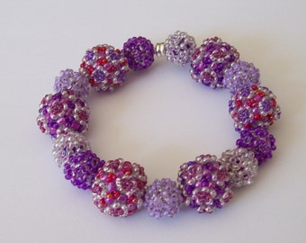 May include: A purple and red beaded bracelet with a silver clasp. The beads are round and have a textured surface.