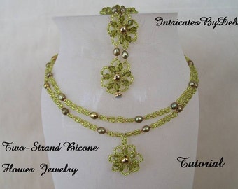 May include: A two-strand green and gold bicone flower necklace with a matching pendant. The necklace is on a white display stand. The text "Intricates By Deb" and "Two-Strand Bicone Flower Jewelry Tutorial" is visible in the image.
