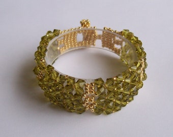 May include: A green and gold beaded bracelet with a clear plastic base. The bracelet is made with small, faceted beads and gold beads.