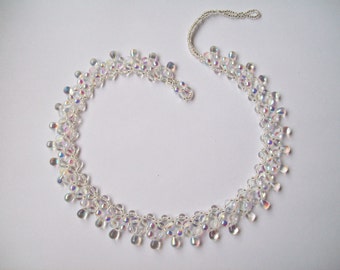 May include: A delicate iridescent crystal necklace with a silver chain. The necklace is made of small, faceted beads that are strung together in a pattern that creates a cascading effect.