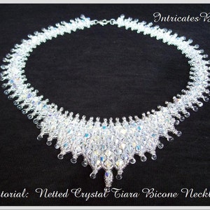 Op de afbeelding: Een delicate kristallen ketting met een gaasontwerp. De ketting is gemaakt van heldere bicone-kristallen en heeft een traanvormige hanger. De ketting ligt op een zwarte achtergrond.  Tutorial: Geweven Crystal Tiara Bicone Ketting