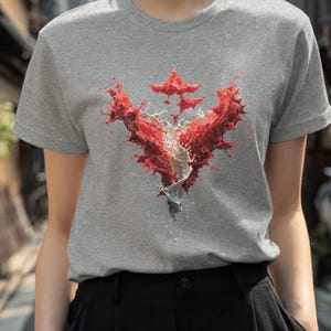 May include: A grey t-shirt featuring a vibrant red and white abstract design. The graphic appears to be a stylized splash or burst of color. The word "Grey" is printed at the bottom of the image.