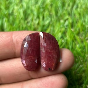 Könnte beinhalten: Zwei facettierte, halbkreisförmige lose Edelsteine in tiefroter Farbe mit polierter Oberfläche. Die Steine haben eine flache, gerade Kante und eine abgerundete Außenkante sowie einen geometrischen Schliff, der das Licht auf den Oberflächen reflektiert.