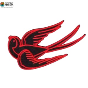Może przedstawiać: Czarna i czerwona naszywka z haftem przedstawiająca stylizowaną jaskółkę w locie. Naszywka ma szczegółowy wzór z czerwonym obrysem skrzydeł i ogona ptaka na czarnym korpusie. Naszywka jest na białym tle.