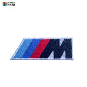May include: Embroidered patch of the BMW M logo. The patch is rectangular with a white border. The logo features light blue, dark blue, red, and black stripes, and a white "M" on a black background. The text "EVERY DAY PATCHES" is in the top left corner.