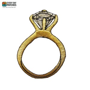 May include: Embroidered patch of a gold engagement ring with a large, clear diamond-shaped stone. The ring has a detailed, textured appearance, with the words "EVERY DAY PATCHES" and "STYLE THAT STICKS EVERY DAY" in the upper left corner.