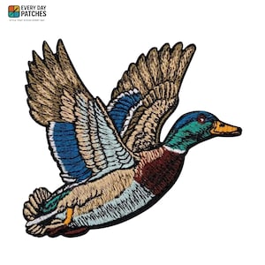Może przedstawiać: Haftowana naszywka przedstawiająca lecącego kaczora. Naszywka prezentuje szczegółowe przeszycia w odcieniach brązu, błękitu, zieleni i kasztanowego. Tekst "EVERY DAY PATCHES" jest widoczny w lewym górnym rogu.