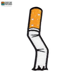 Peut inclure: Écusson brodé en forme de mégot de cigarette plié. Le patch présente un filtre blanc, une section de tabac de couleur beige et un contour noir. Le patch porte le texte "EVERY DAY PATCHES" en haut.
