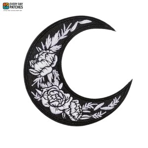 May include: A crescent moon shaped embroidered patch featuring a black background with white thread detailing. The design includes white floral motifs and leafy sprigs arranged along the curve of the moon. The text EVERY DAY PATCHES is visible.