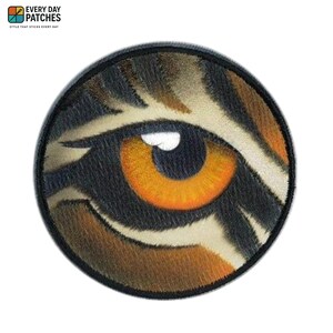 May include: Round patch featuring a detailed tiger eye with orange iris, white highlights, and black, brown, and tan fur-like textures. The patch has a black border and the text "EVERY DAY PATCHES" and "STYLE THAT STICKS EVERY DAY".