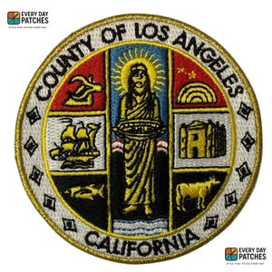 May include: Embroidered patch featuring the County of Los Angeles seal. The circular patch has a white border with gold stitching. The seal includes a central figure, a ship, a building, and a cow, with the text "COUNTY OF LOS ANGELES CALIFORNIA".