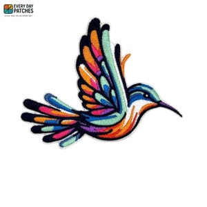 Op de afbeelding: Geborduurde kolibrie-patch met een levendig ontwerp. De vogel heeft een kleurrijk palet van blauw, oranje, roze en groen, met zwarte contouren. De patch heeft de tekst "EVERY DAY PATCHES" en "STYLE THAT STICKS EVERY DAY".