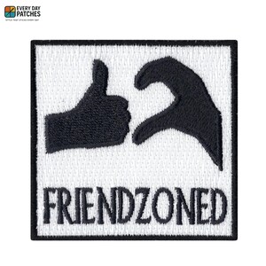 May include: Embroidered patch with a white background and a black border. The patch features a black thumbs-up hand gesture next to a hand forming a heart shape. The word "FRIENDZONED" is embroidered in black below the hands.