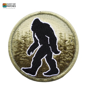 Op de afbeelding: Ronde geborduurde patch met een zwart silhouet van Bigfoot die door een bos loopt. De patch heeft een bruine rand en een groen-bruine achtergrond. De tekst "EVERY DAY PATCHES" en "STYLE THAT STICKS EVERY DAY" staat bovenaan.
