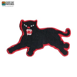 Può includere: Toppa ricamata raffigurante una pantera nera con contorno rosso, che ringhia con i denti bianchi. La toppa include il testo "EVERY DAY PATCHES" e "STYLE THAT STICKS EVERY DAY" nell'angolo in alto a sinistra.