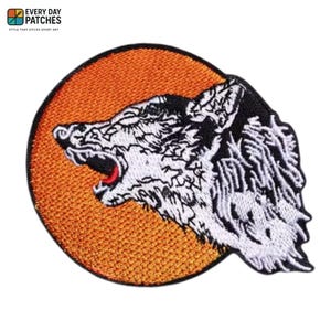 Pode incluir: Patch bordado com a imagem de uma cabeça de lobo rosnando com pelo branco e detalhes em preto, sobre um fundo circular laranja. O patch inclui o texto "EVERY DAY PATCHES" na parte superior.