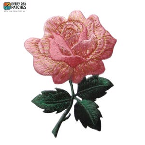 May include: Embroidered patch of a pink rose with gold detailing. The rose is intricately stitched and set against a white backdrop. Green leaves and stem complete the floral design. The patch includes the text "EVERY DAY PATCHES" and "STYLE THAT STICKS EVERY DAY".