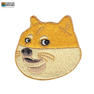 Op de afbeelding: Geborduurde patch met de Doge-meme, een Shiba Inu-hond met een glimlachende uitdrukking. De patch is voornamelijk geel en beige, met zwarte en witte details. De tekst "EVERY DAY PATCHES" staat bovenaan.