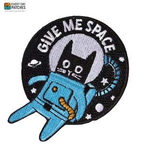 Op de afbeelding: Ronde geborduurde patch met een zwarte kat in een blauw ruimtepak, omringd door de woorden "GIVE ME SPACE". Het ontwerp bevat sterren en een planeet, ideaal voor ruimtevaartliefhebbers.