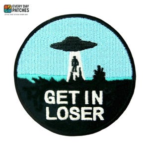 Può includere: Toppa rotonda con bordo nero. Raffigura un cielo azzurro chiaro con un UFO nero e una figura aliena. Il testo "GET IN LOSER" è in lettere bianche sotto.