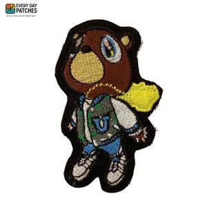 May include: Embroidered patch featuring a brown bear wearing a varsity jacket, blue jeans, and white sneakers. The bear has a gold chain and a yellow backpack. The patch is outlined in black and includes the text "EVERY DAY PATCHES".