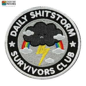 May include: Circular embroidered patch with the text "DAILY SHITSTORM SURVIVORS CLUB". The design features a black cloud with a sad face, rainbows, lightning bolts, and white clouds on a black background.