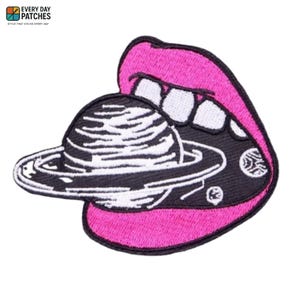 Può includere: Toppa ricamata con un design stilizzato di una bocca con labbra rosa brillante, aperta per rivelare un interno nero con un oggetto simile a un pianeta. Il pianeta ha dettagli bianchi. La toppa ha il testo "EVERY DAY PATCHES" in alto.