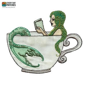 May include: Embroidered patch showing a mermaid reading in a teacup. The mermaid has green hair and tail, and the teacup is white with a decorative handle. The patch includes the text "EVERY DAY PATCHES" at the top, ideal for clothing or accessories.