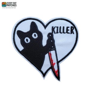 Peut inclure: Écusson brodé en forme de cœur avec un chat noir tenant un couteau ensanglanté. Le mot "KILLER" est au-dessus du couteau. L'écusson a un fond blanc et une bordure noire.