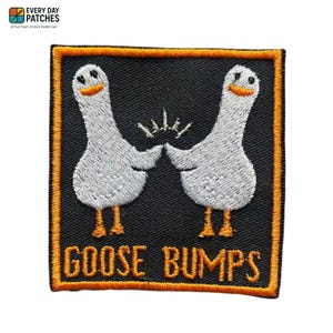 Op de afbeelding: Geborduurde patch met twee witte ganzen, oranje snavels en poten, die elkaar een high-five geven. De patch heeft een zwarte achtergrond met een oranje rand. De woorden "GOOSE BUMPS" zijn oranje geborduurd.