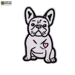 May include: An embroidered iron-on patch featuring a white French bulldog with black outlines and details. The dog is depicted in a sitting position with a small pink heart stitched on its chest. The design has a clean white background.