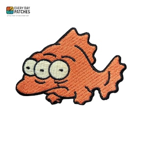 May include: Embroidered orange fish patch with three eyes and a black outline. The patch has a textured appearance and the text "EVERY DAY PATCHES" and "STYLE THAT STICKS EVERY DAY" in the upper left corner.