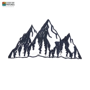 Puede incluir: Un parche bordado con un diseño de cordillera en hilo azul marino oscuro y blanco. El gráfico muestra tres picos irregulares con un denso bosque de pinos en la base, sobre un fondo blanco liso.