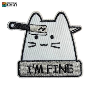 Può includere: Toppa ricamata raffigurante un gatto dei cartoni animati con una mannaia sulla testa. Il gatto è grigio chiaro con dettagli neri e la scritta "I'M FINE" in nero. La toppa ha un bordo nero ed è progettata per essere stirata.