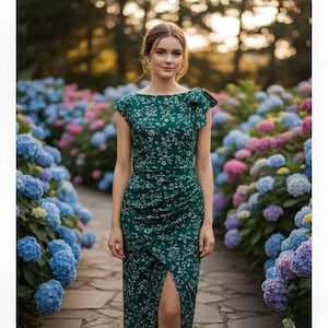 May include: A woman wearing a dark green dress with a white floral pattern, standing on a stone path. The dress has a high slit and a bow detail on the shoulder. The background features a garden with colorful hydrangeas.