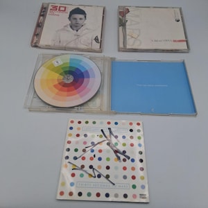 May include: Several CD cases are displayed, showcasing music albums. One case features a portrait of a person, while another displays a color wheel. The album covers have text and graphics, including the band name "30 Seconds to Mars".